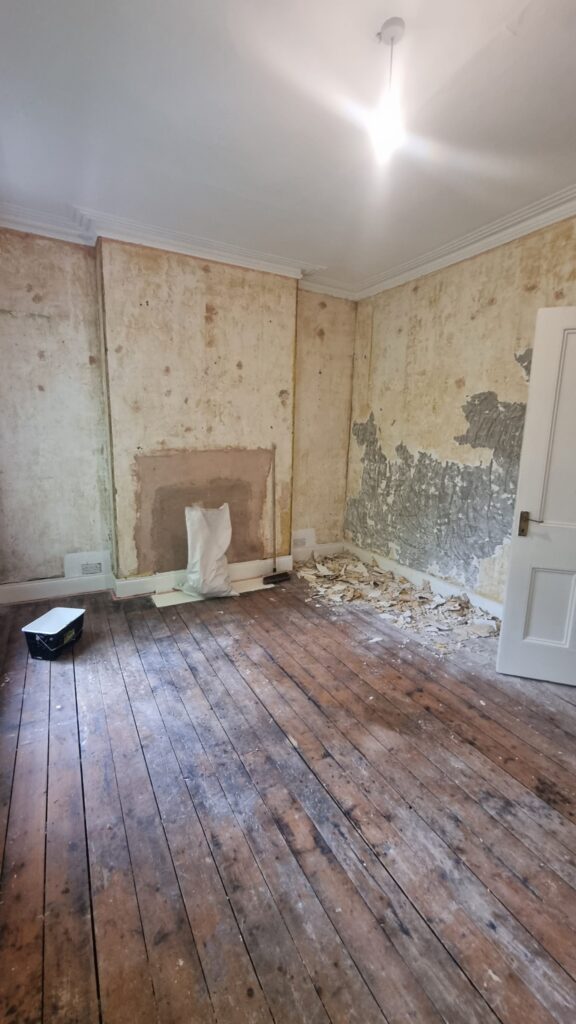 Bedroom stripped back to bare plaster walls and wooden floorboards during a home renovation
