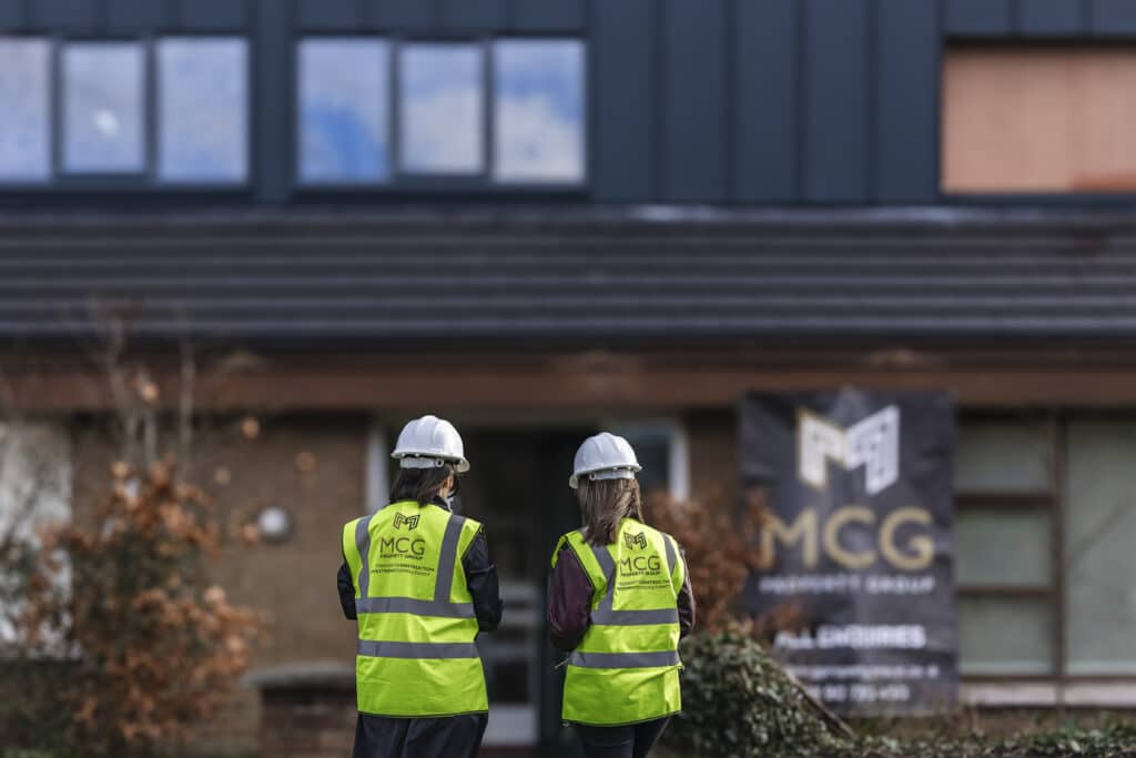 Two MCG Property Group team members in hi-vis and hard hats outside a renovation project beside MCG signage